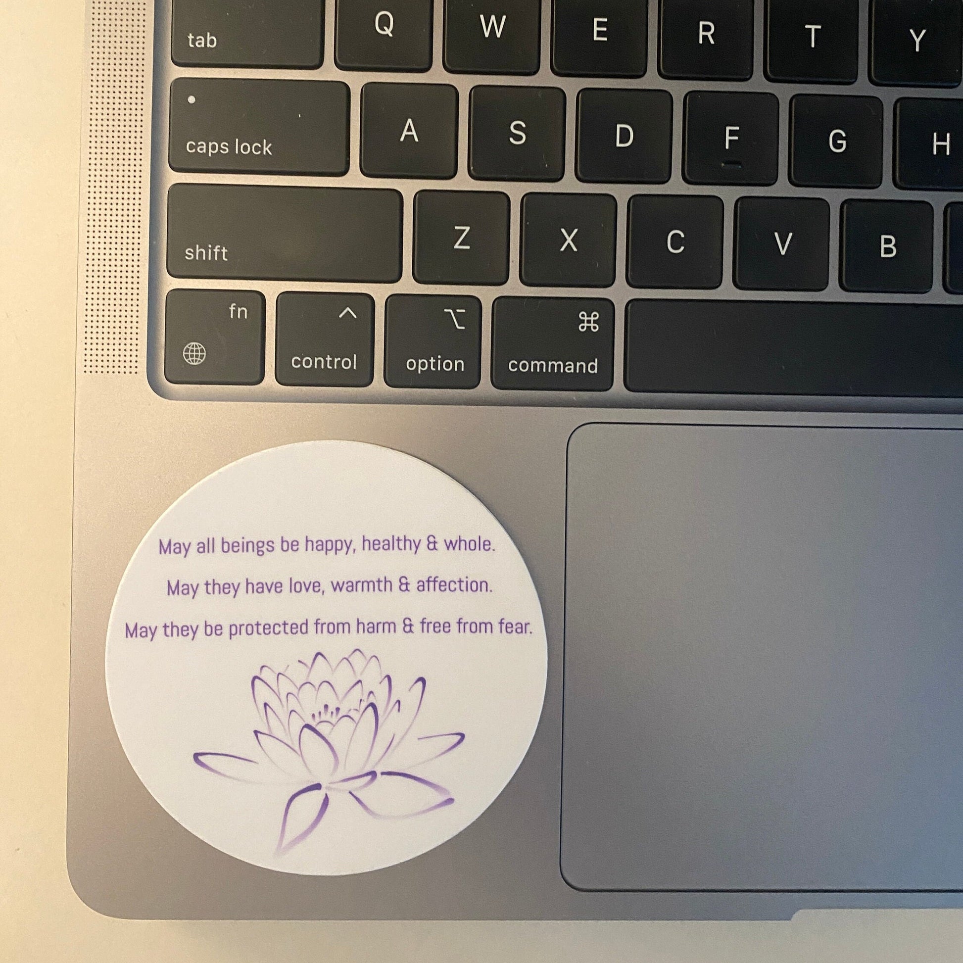Laptop keyboard with a 3" circular sticker with Buddhist prayer and a lotus design.