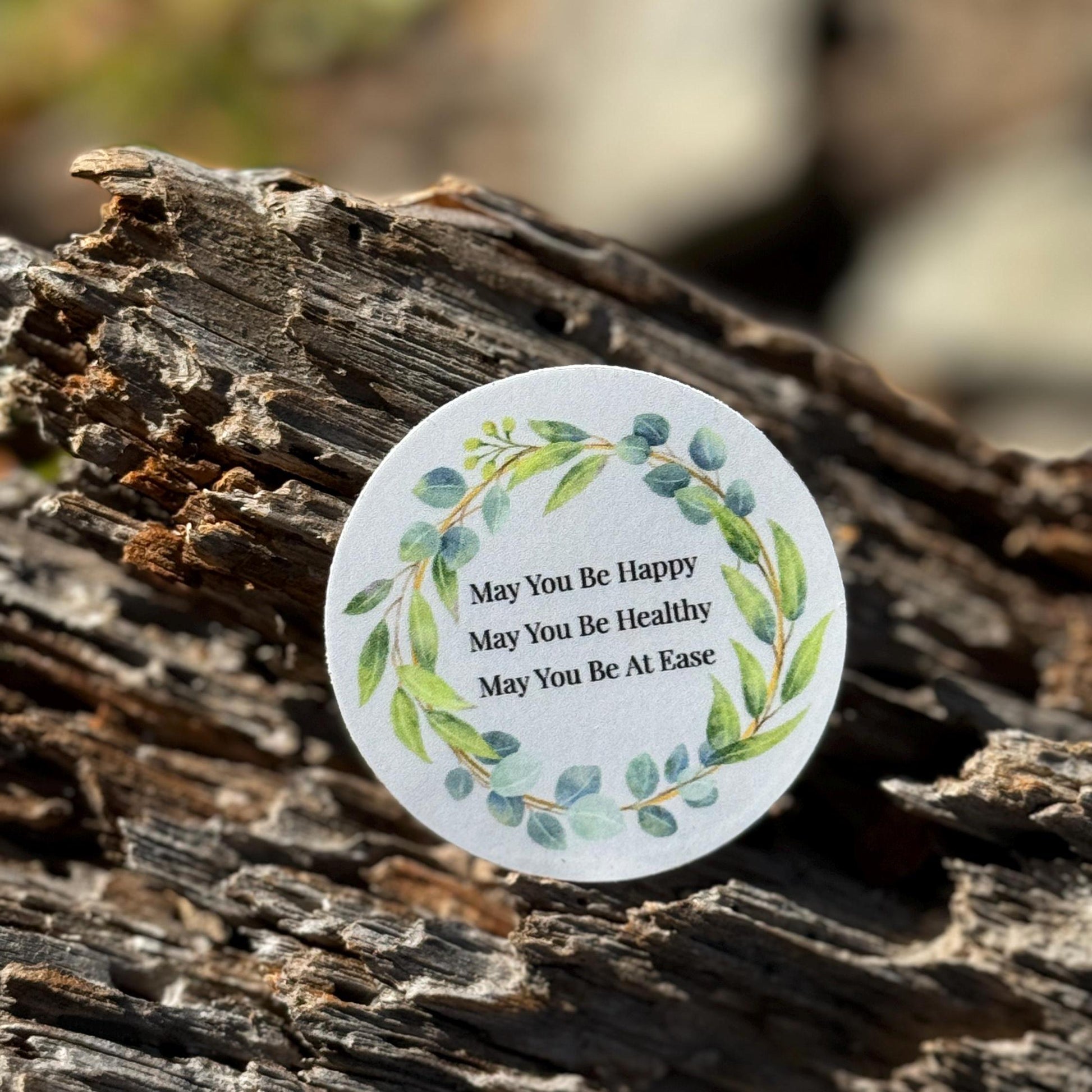 2" round blue sticker with Buddhist mettā prayer text, may you be happy may you be healthy may you be at ease. Sitting on a tree branch.