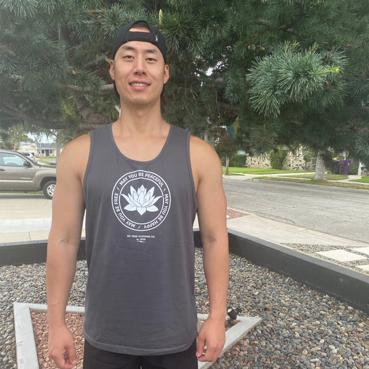Person wearing a gray tank top with a lotus and the text, MAY YOU BE PEACEFUL MAY YOU BE HAPPY MAY YOU BE FREE, design outdoors.