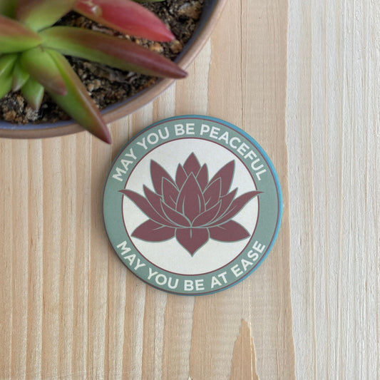 3.5" lotus flower magnet with the metta prayer, 'may you be peaceful may you be at ease' it is next to a succulent plant.