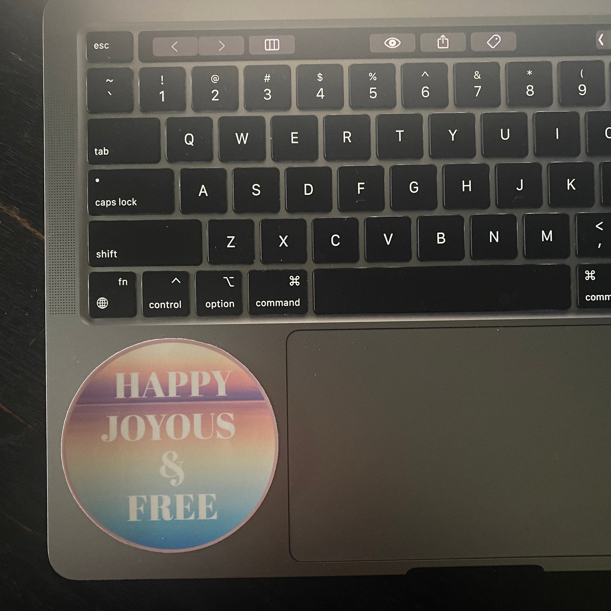 Laptop keyboard with a 'Happy Joyous & Free' sticker on the trackpad.