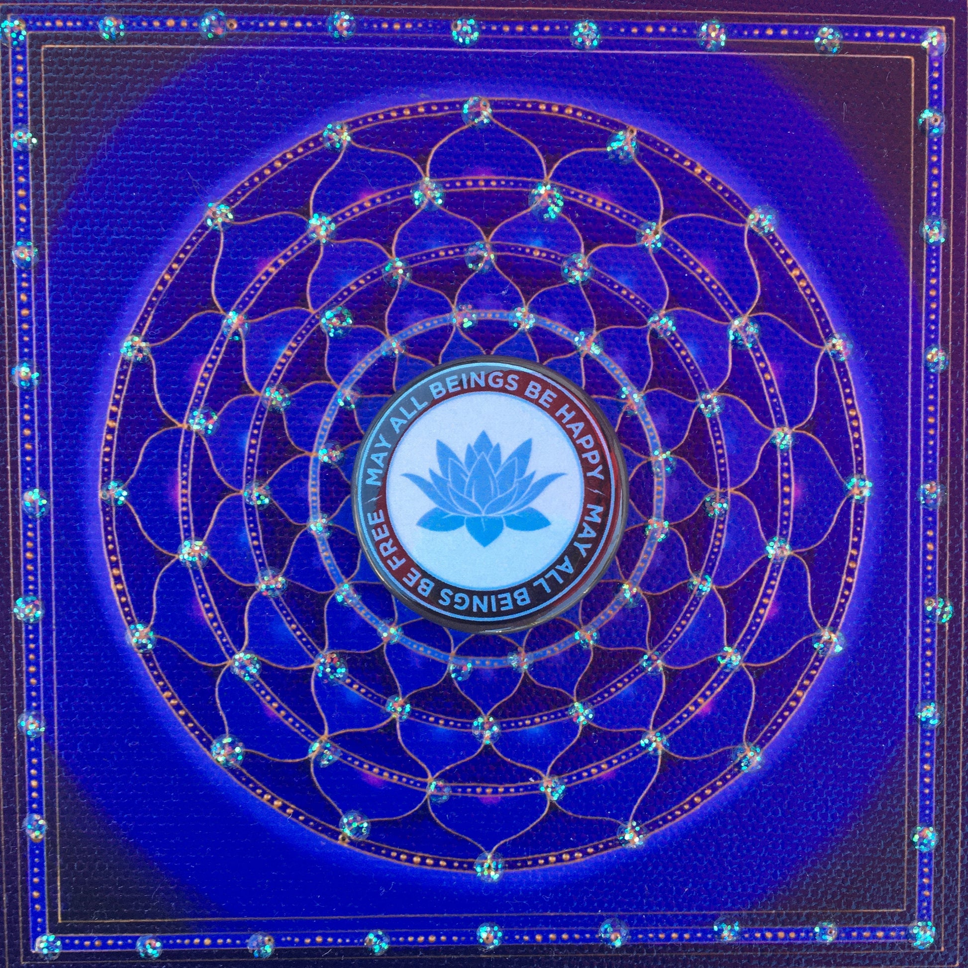 Decorative blue and black button with a lotus symbol and 'All Beings Be Happy May All Beings Be Free' text on a blue background.