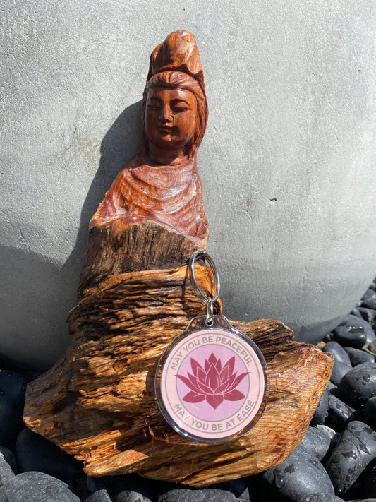 Wooden Bodhisattva seated figure with a 2" pink lotus keychain that reads, may you be peaceful may you be at ease on a stone surface.