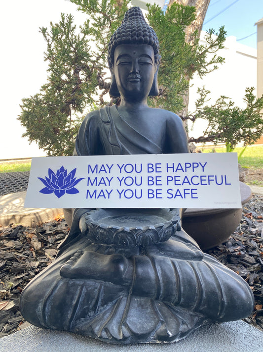 Buddha statue holding a White and blue buddhist prayer bumper sticker that reads, MAY YOU BE HAPPY MAY YOU BE PEACEFUL MAY YOU BE SAFE.