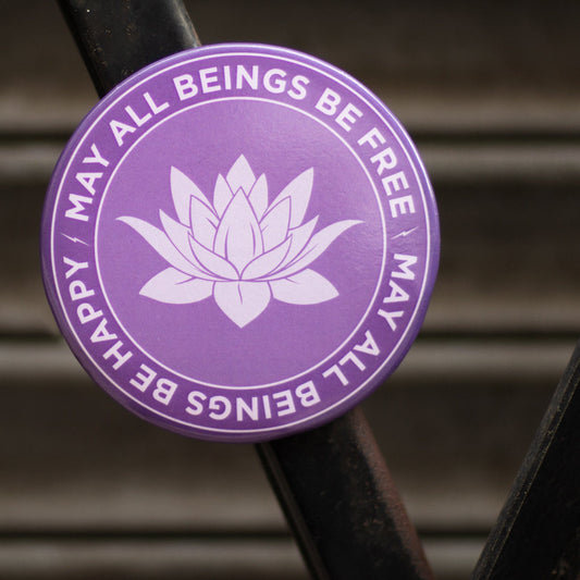 Purple magnet with lotus design and text, may all beings be free may all beings be happy, on a metal surface.