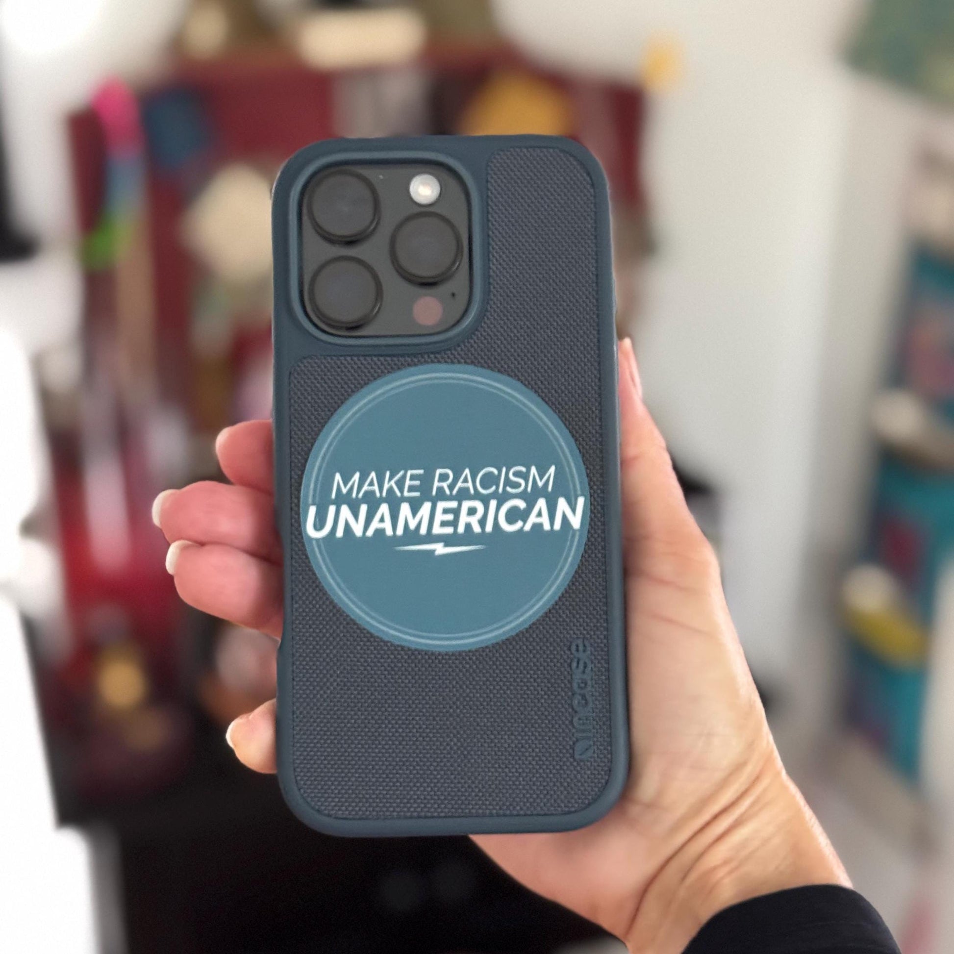 Phone case with 'Make Racism Unamerican' text held by a hand against a blurred background.