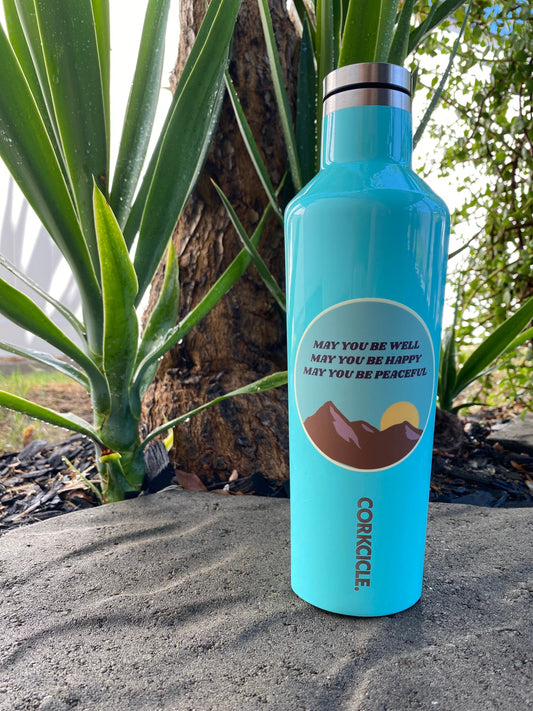 Blue Corkcicle water bottle with a Buddhist loving kindness mantra sticker that reads,  may you be well may you be happy may you be peaceful, in a natural background.