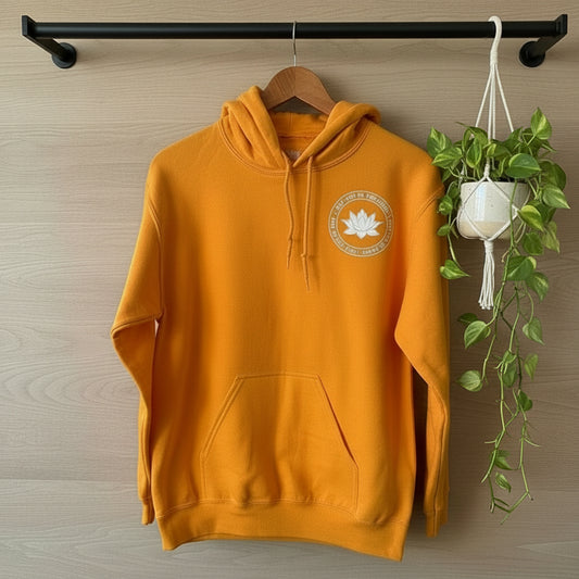 Orange hoodie with a lotus that reads, may you be peaceful-free-happy, on a black clothing rod against a neutral background.