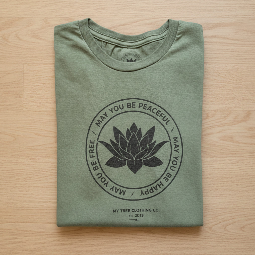 Folded green t-shirt with a black lotus flower design and the metta prayer on a wooden background.