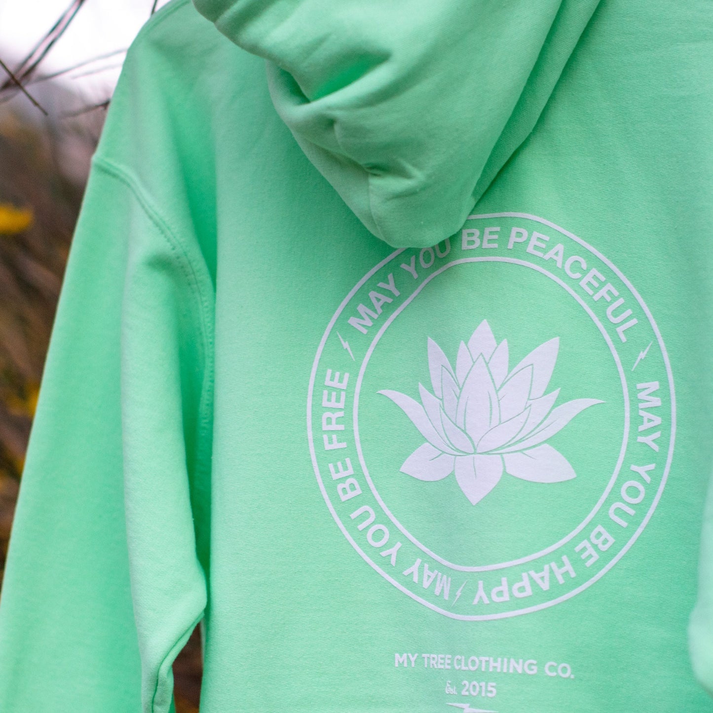 Green hoodie with a white lotus flower design and text on the back, brand 'My Tree Clothing Co.' visible.