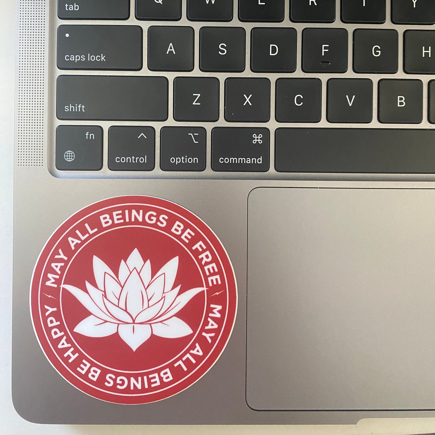 Laptop keyboard with a red and white sticker featuring a lotus flower design and the metta prayer on the palm rest area.