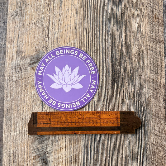 Four inch round purple lotus sticker with the words, MAY ALL BEINGS BE FREE-MAY ALL BEINGS BE HAPPY surrounding it. 